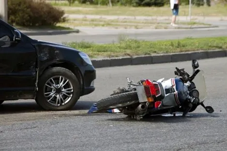 A motorcycle and car accident on the side of the road.